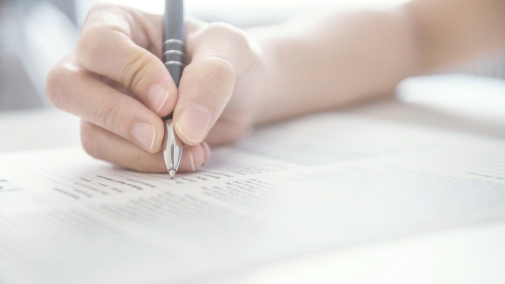 Person with pen completing paperwork.